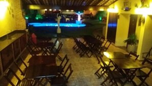 A restaurant with outdoor seating, a pool, and a bar area. - Paratibela Pousada (Anchieta)