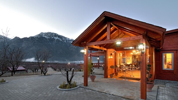 A wooden building with a covered entrance, potted plants, and a mountainous backdrop. - Villa Rustica (Konitsa)
