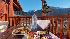 A wooden deck with a table set for a meal, a water bottle, and a view of snow-capped mountains. - Villa Rustica (Konitsa)