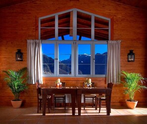 A wooden dining room with a large window overlooking a mountainous landscape.