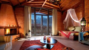 A cozy log cabin interior with a fireplace, a comfortable seating area, and a view of mountains through large windows. - Villa Rustica (Konitsa)