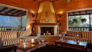 A cozy log cabin interior with a fireplace, striped sofas, and a wooden ceiling. - Villa Rustica (Konitsa)