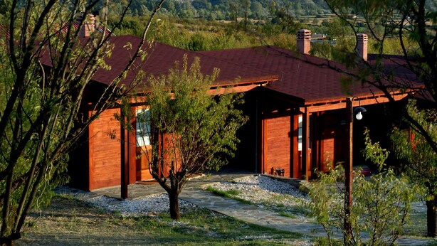A rustic wooden cabin with a red roof, surrounded by trees and a gravel path. - Villa Rustica (Konitsa)