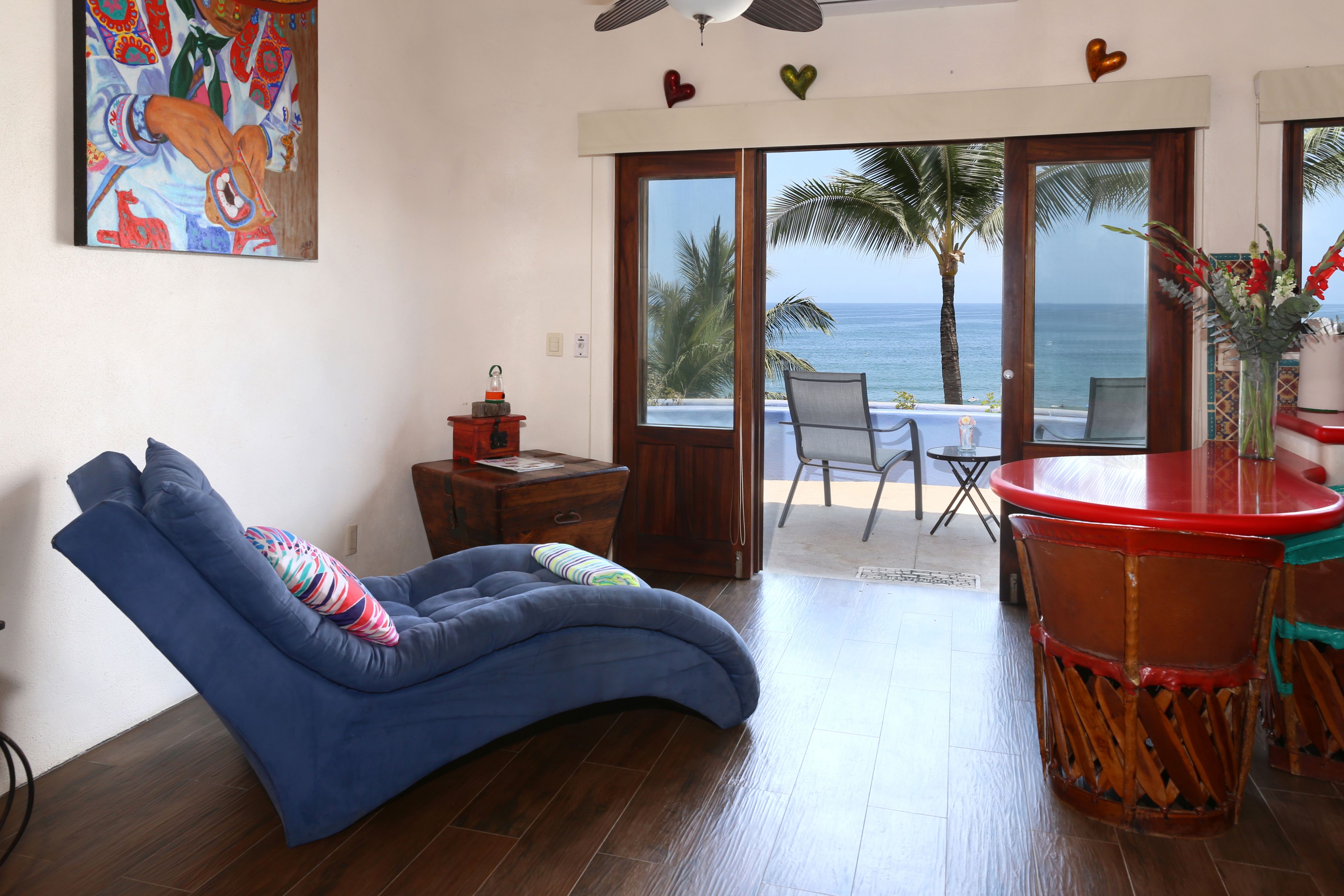Una habitación con un sofá azul curvo, una mesa de centro de madera y vista al océano a través de un ventanal corredero.