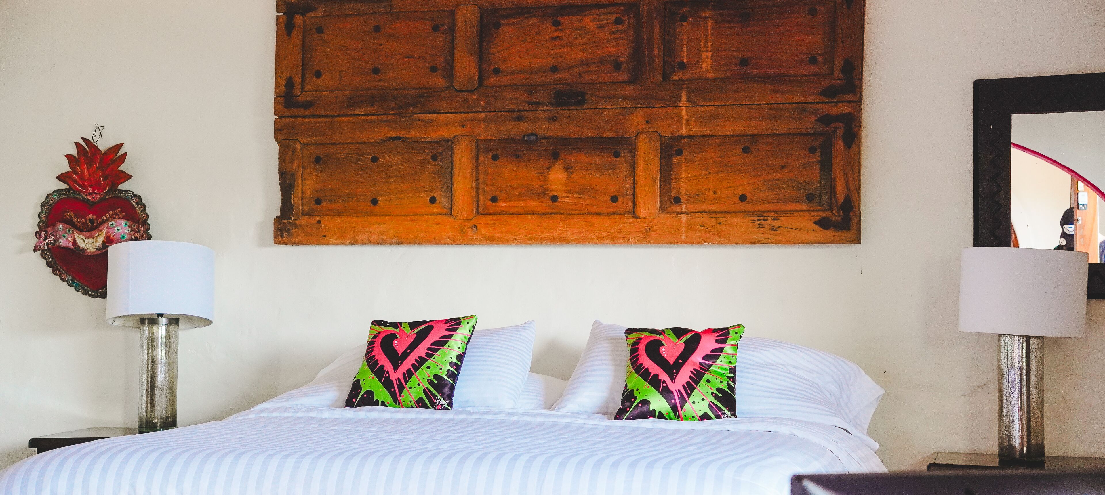 A bed with striped bedding, two heart-patterned pillows, a wooden headboard, and two bedside lamps.