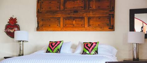 A bed with striped bedding, two heart-patterned pillows, a wooden headboard, and two bedside lamps.
