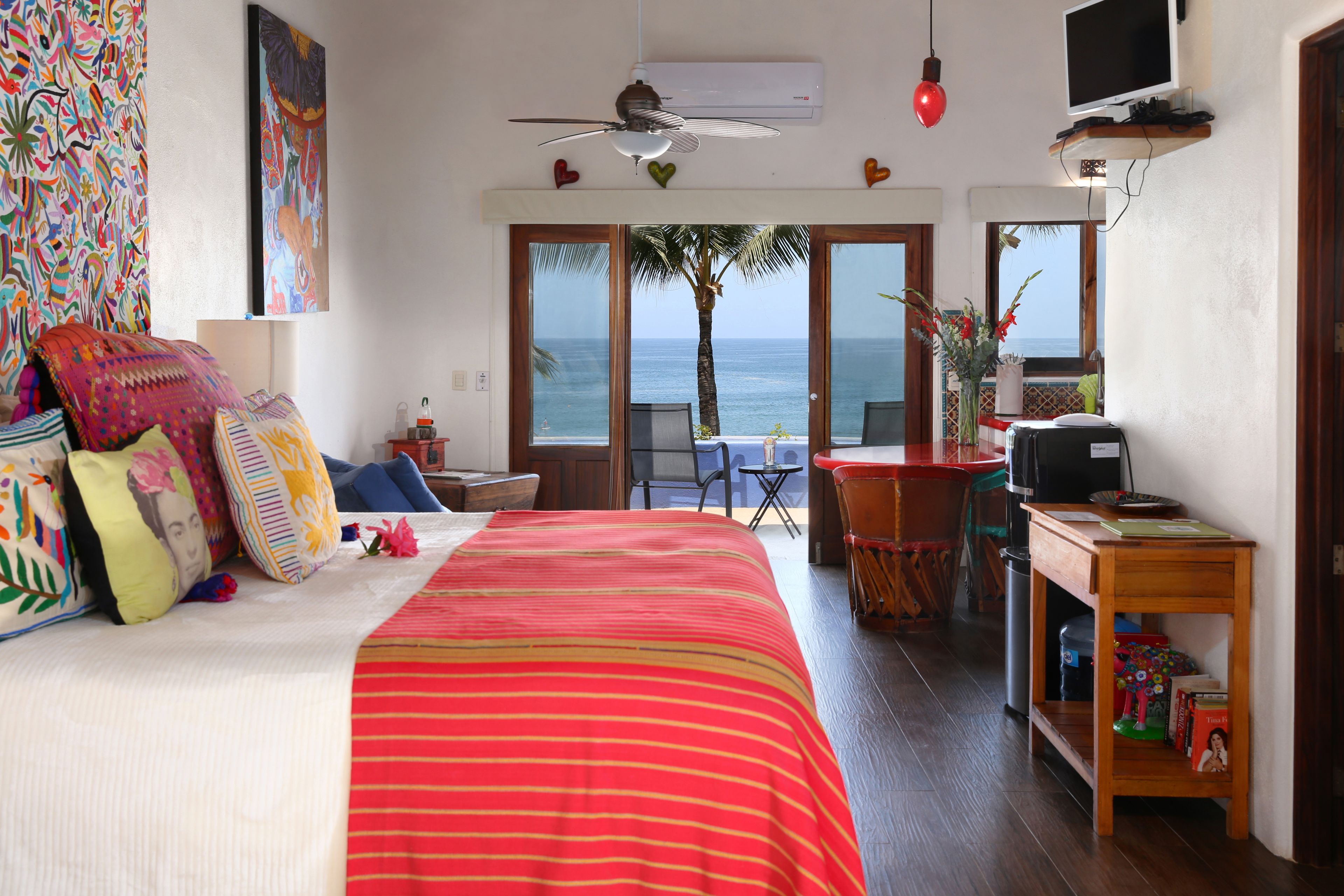 A bedroom with a bed, a desk, a chair, and a view of the ocean.