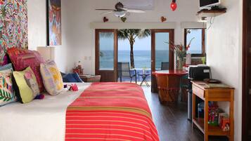 A bedroom with a bed, a desk, a chair, and a view of the ocean.