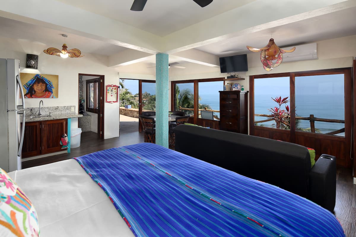 Une chambre spacieuse avec un grand lit, une vue sur la mer, un balcon et un coin cuisine.