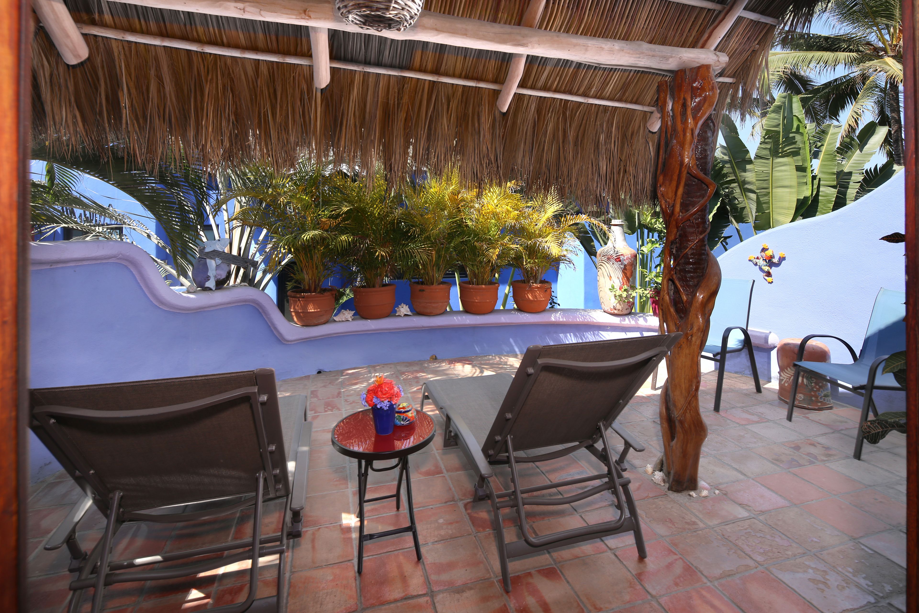 A covered patio with potted plants, a table, and two chairs.