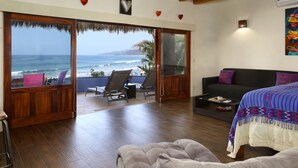A room with a wooden floor, a bed, a sofa, and a view of the ocean. - Casa Pata Salada (Sayulita)