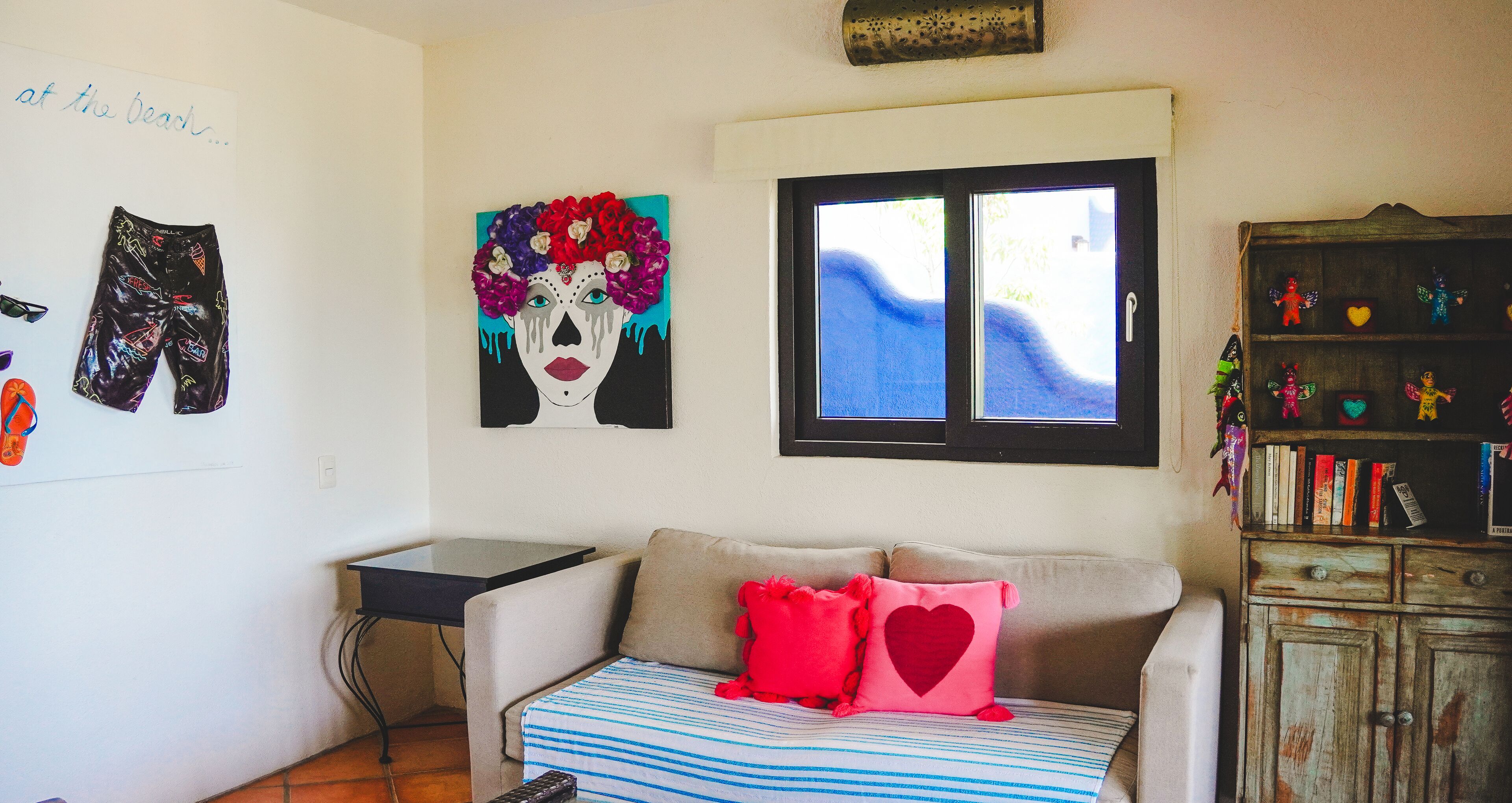 Una habitación con sofá, ventana, una pared con obras de arte y estantería.