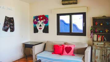 Una habitación con sofá, ventana, una pared con obras de arte y estantería.