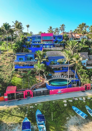 Un hôtel à plusieurs étages doté d’une piscine, entouré de palmiers et de bâtiments bleus.
