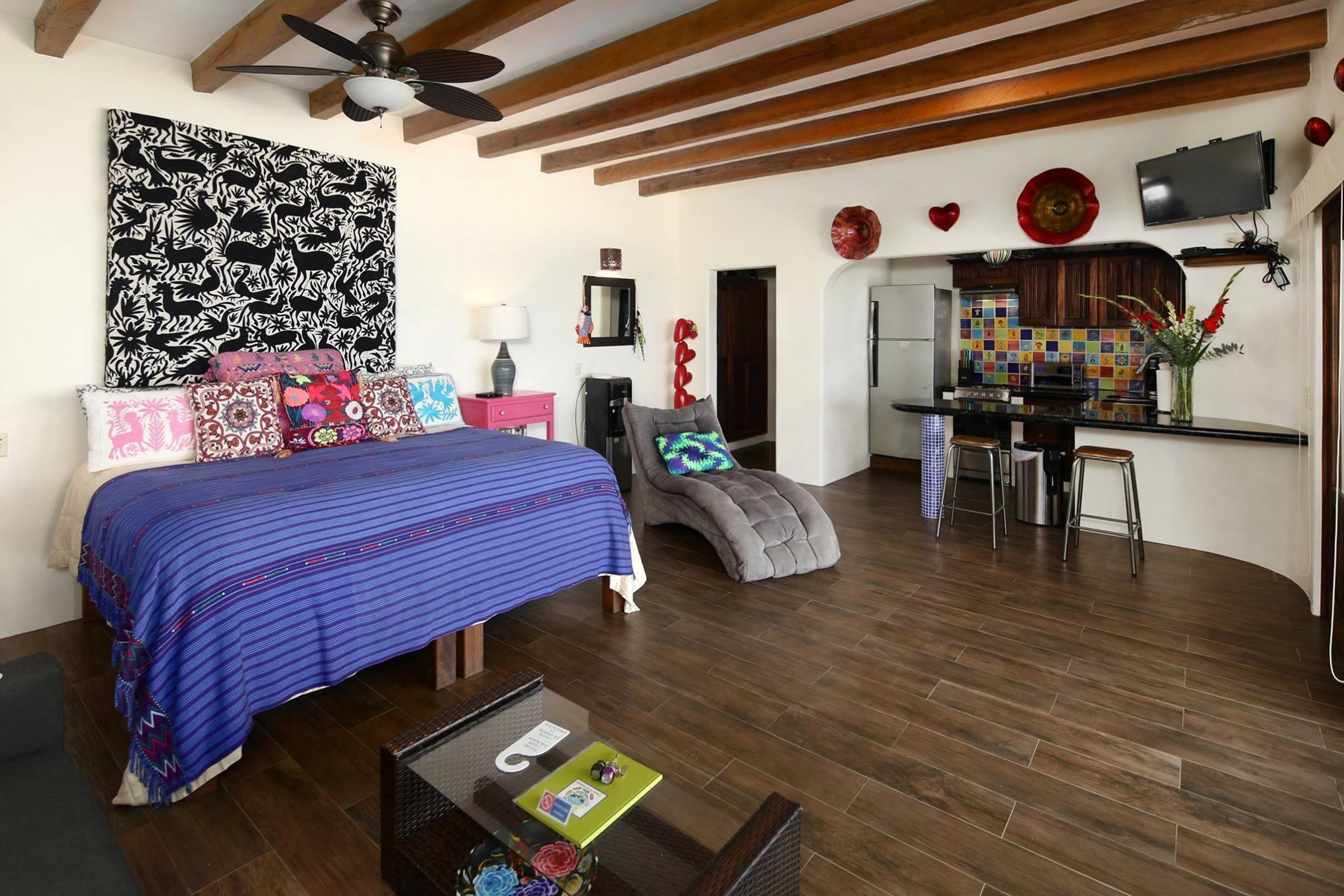 A bedroom with a large bed, a desk, and a kitchenette.