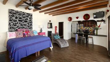 A bedroom with a large bed, a desk, and a kitchenette.