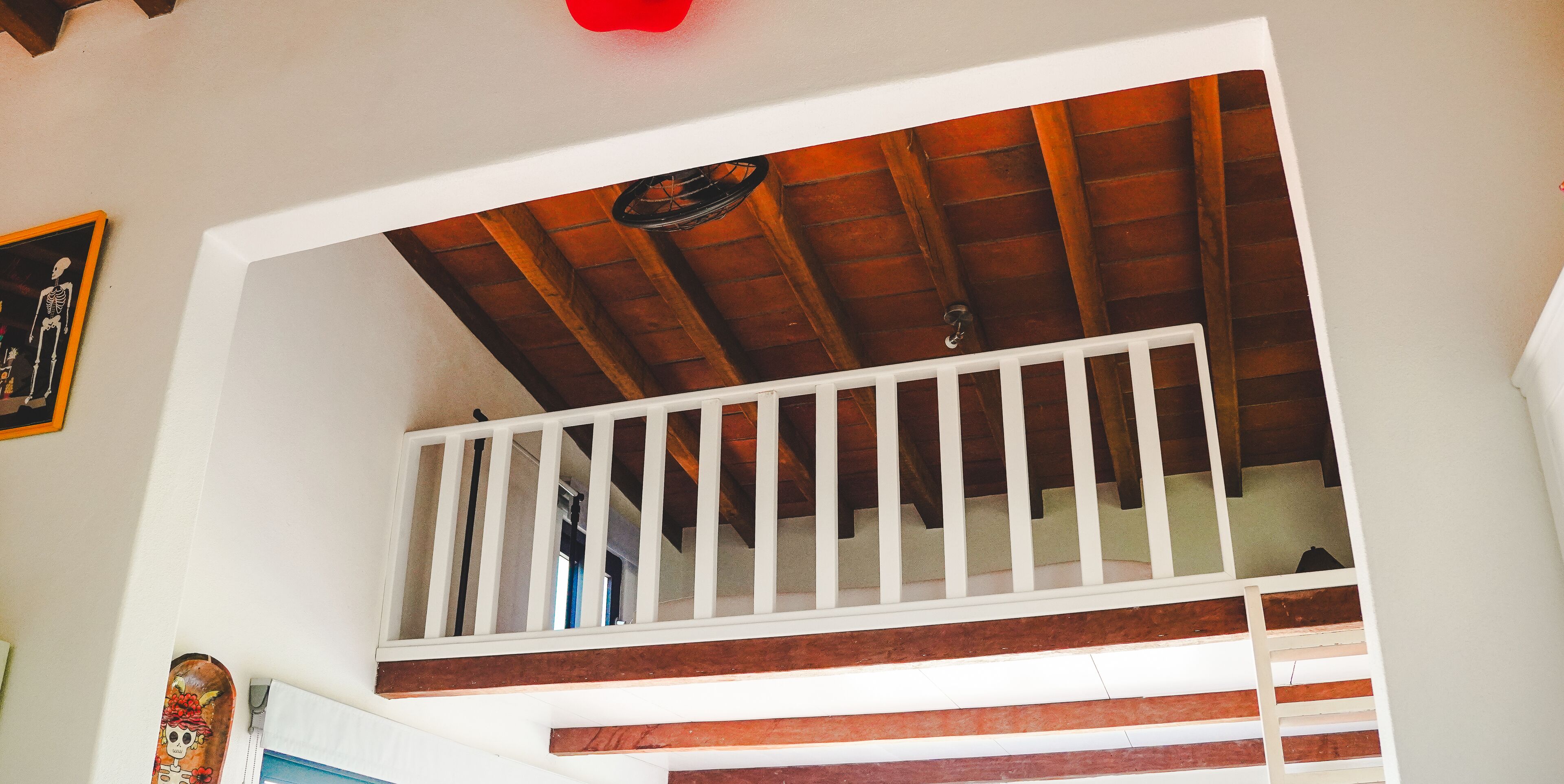 A staircase with wooden steps and white railings, leading to a room with a wooden ceiling and a red light fixture.