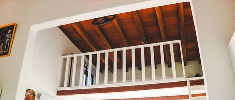 A staircase with wooden steps and white railings, leading to a room with a wooden ceiling and a red light fixture.