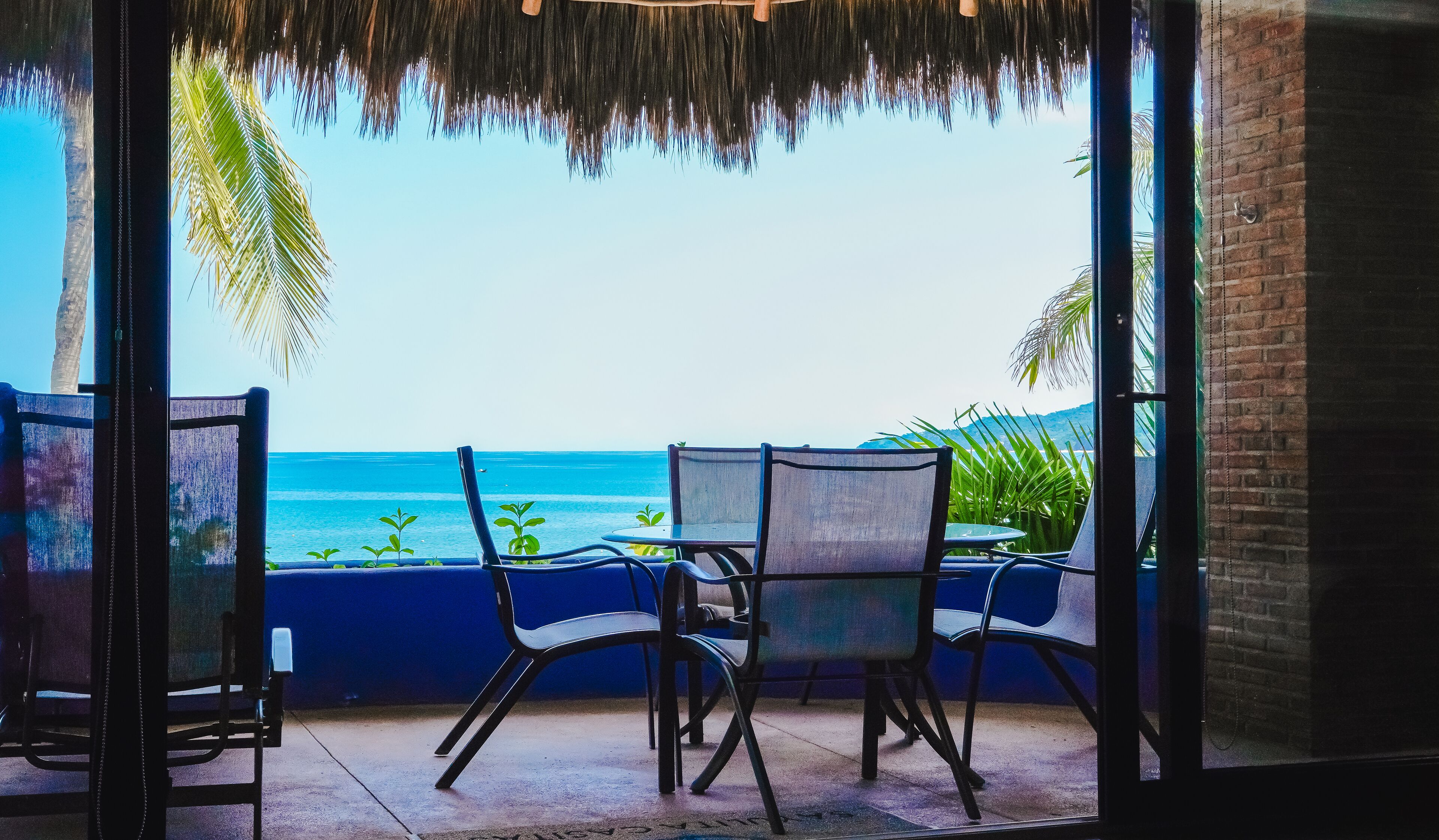 A view from a room with a glass door to the ocean, featuring two chairs and a small table.
