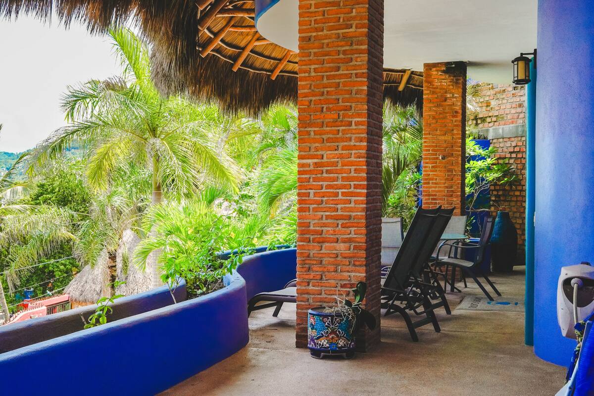 Un espace extérieur abrité, doté de piliers en briques, de jardinières bleues et de sièges d’extérieur.