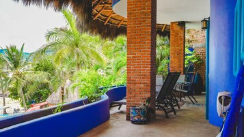 Un espacio al aire libre techado con pilares de ladrillo, macetas azules y mobiliario exterior.