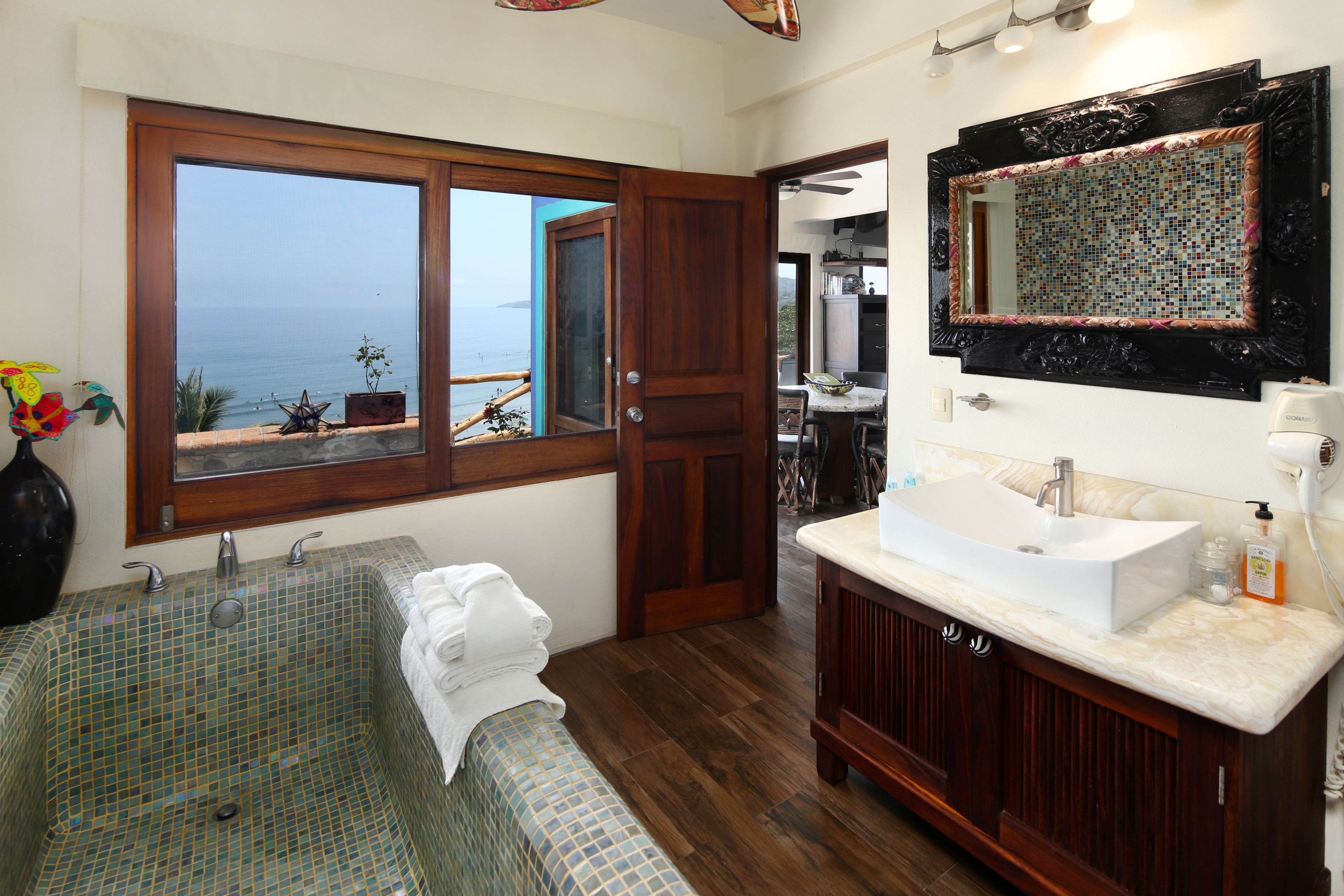 Un baño con un ventanal grande, una bañera, un lavabo y un espejo.