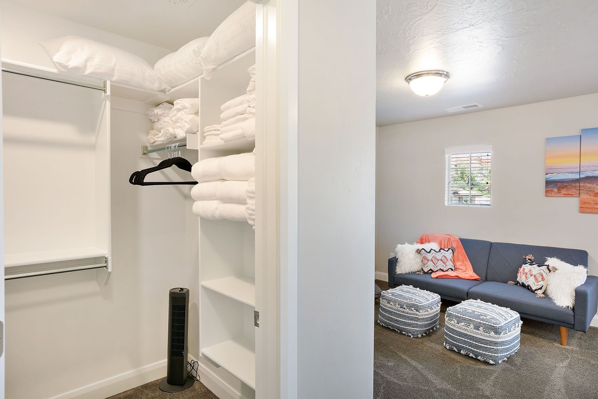 A room with a walk-in closet, a standing heater, a sofa with ottomans, and a window with blinds.
