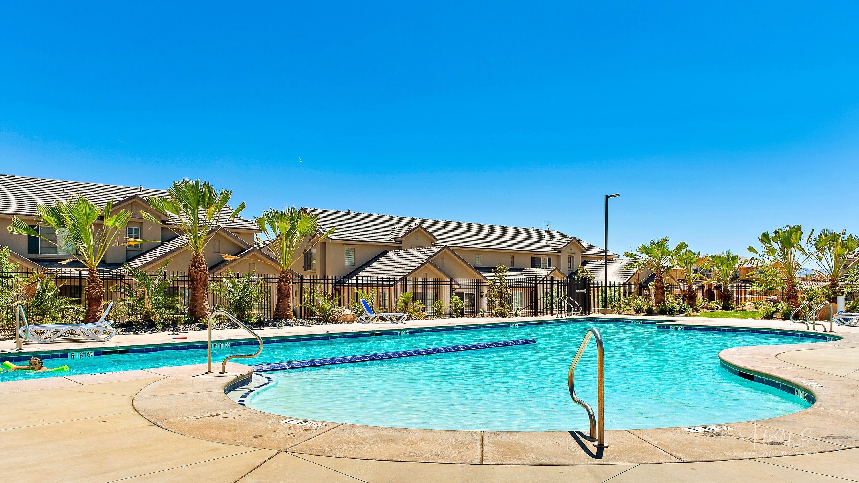 A swimming pool with a clear blue water, surrounded by palm trees and lounge chairs.