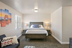 A bedroom with a bed, two bedside tables, a nightstand, a window with blinds, and a wall with three framed pictures. - Southern Adobe by RedAwning (Washington)