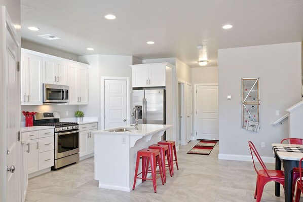 A modern kitchen with white cabinetry, stainless steel appliances, and a central island with red bar stools. - Southern Adobe by RedAwning (Washington)