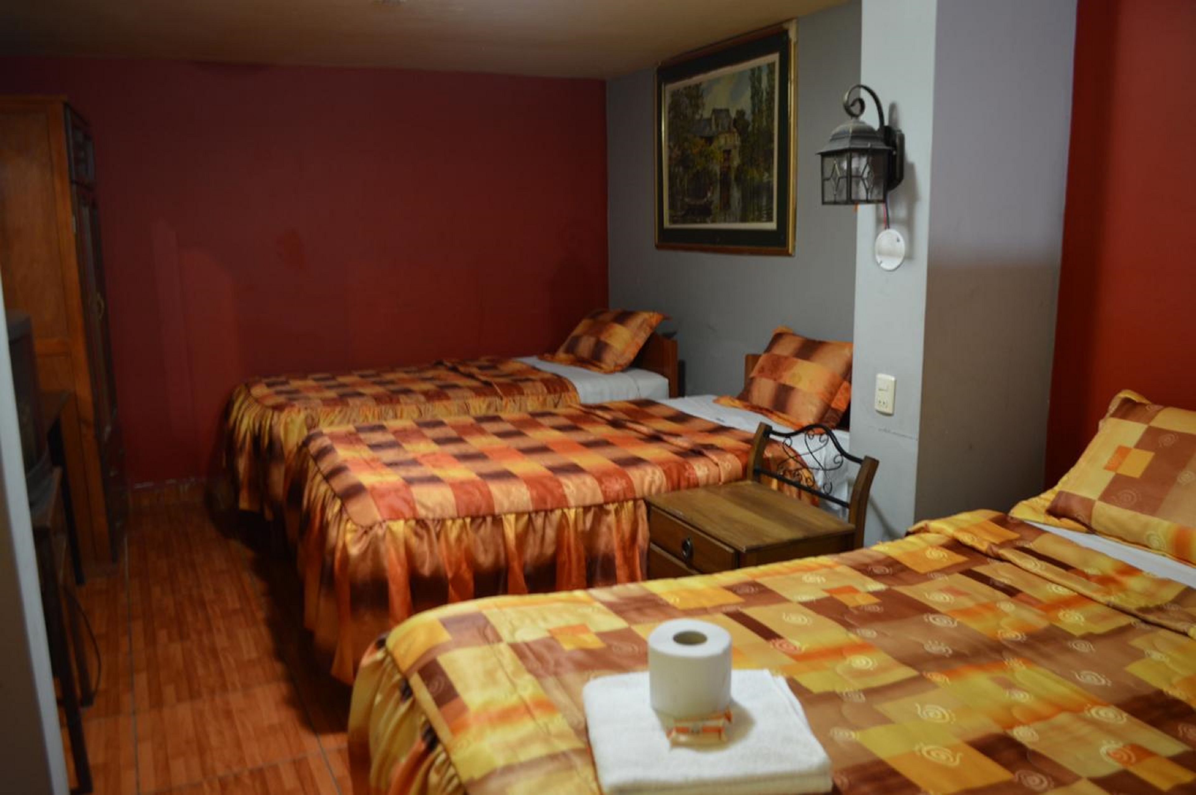 A room with two beds, each with a patterned bedspread, a wooden table, a wall-mounted lamp, and a painting.