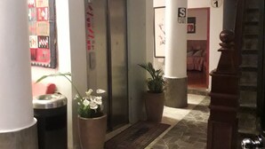 A hallway with a stone floor, potted plants, a trash bin, an elevator, and a staircase. - Hotel El Eden de Adan y Eva (Andahuaylas)