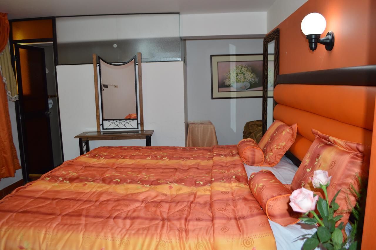 A bedroom with a large bed, a dresser, a mirror, and a wall-mounted light fixture.