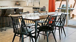 A modern kitchen with white cabinets, a dining area with black chairs, and a large window with blinds. - Red Cliffs by RedAwning (Washington)