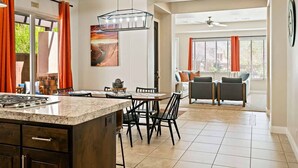 A modern kitchen with a granite countertop, black chairs, and a dining table. There is a large window with orange curtains, a ceiling fan, and a painting on the wall. - Red Cliffs by RedAwning (Washington)