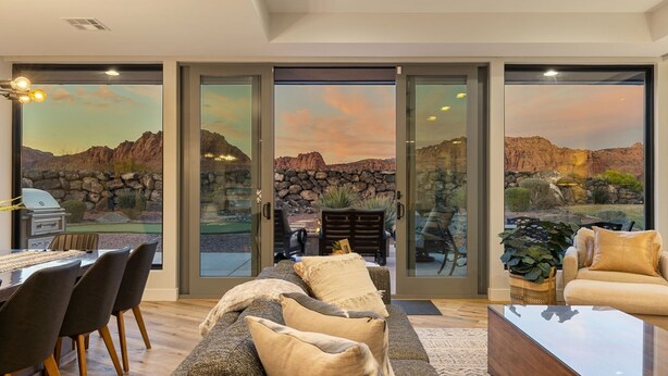 Un salon moderne doté d’une grande porte vitrée donnant sur un patio d’où l’on peut admirer un paysage rocheux et un coucher de soleil.