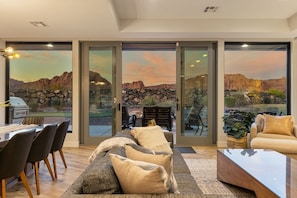 A modern living room with a large glass door leading to a patio with a view of rocky terrain and a sunset. - Snow Canyon Retreat #13 by RedAwning (Ivins)