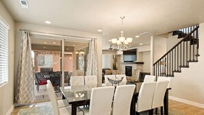 A dining area with a glass table and white chairs, a chandelier, and a staircase. - Sunshine in Paradise #27 by RedAwning (Ivins)