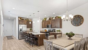 Une cuisine moderne avec des meubles en bois, des appareils électroménagers en acier inoxydable et un coin repas comprenant une grande table et des chaises.