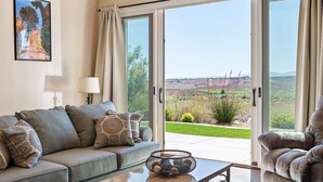 A living room with a sofa, a coffee table, and a view through glass doors to a landscaped outdoor area.