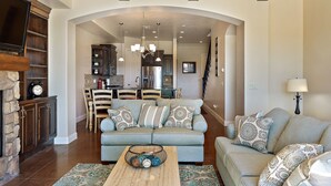A living room with a sofa, coffee table, and a fireplace. There is a kitchen in the background.