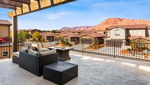 Portico coperto con mobili in vimini, un braciere e vista su una zona residenziale con case e montagne.