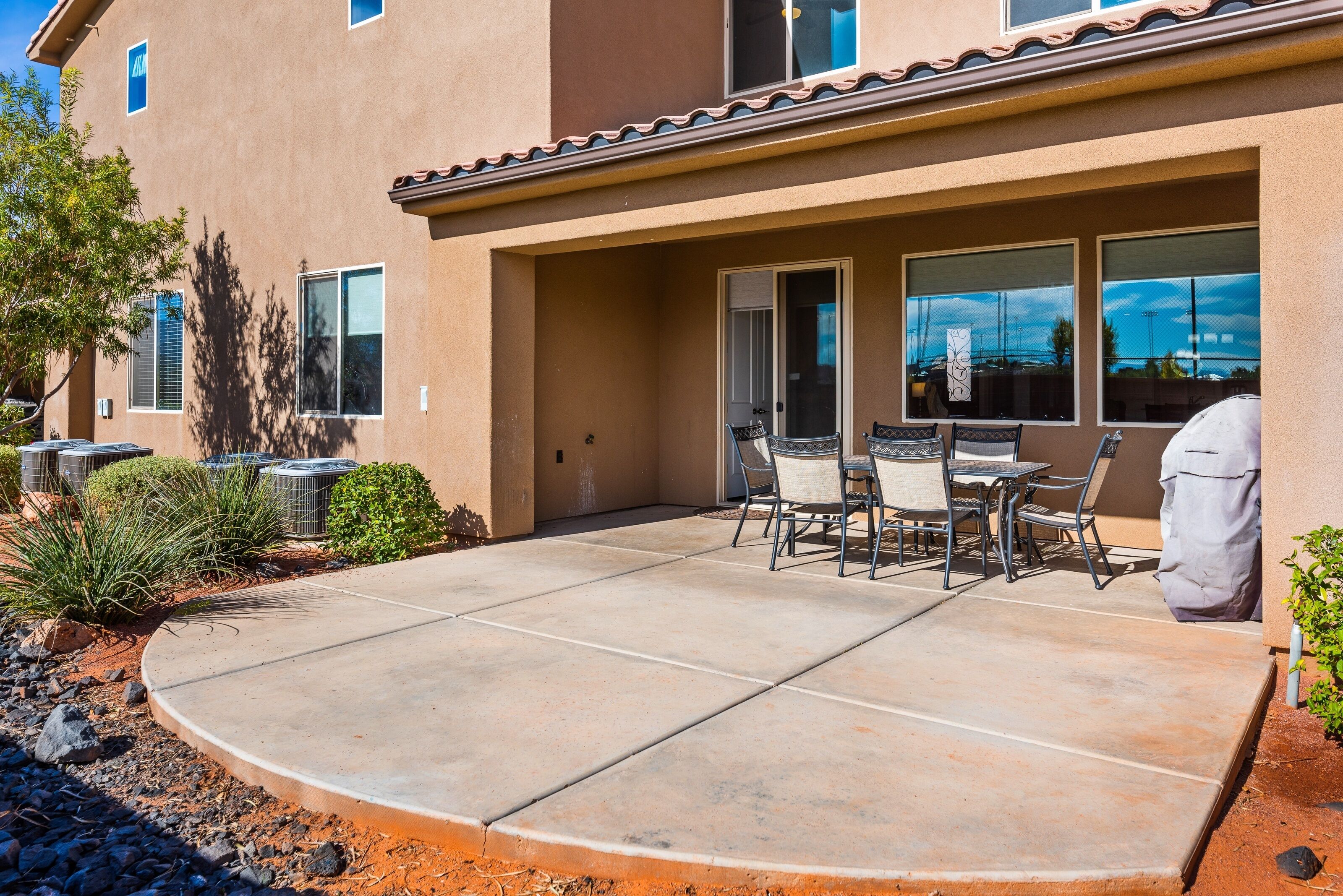 A patio with a concrete floor, outdoor seating, and a covered area with a grill.