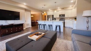 A modern living room with a large flat-screen TV, a dark grey sofa, and a wooden tray with remote controls. - Stella's at Estancia by RedAwning (St. George)