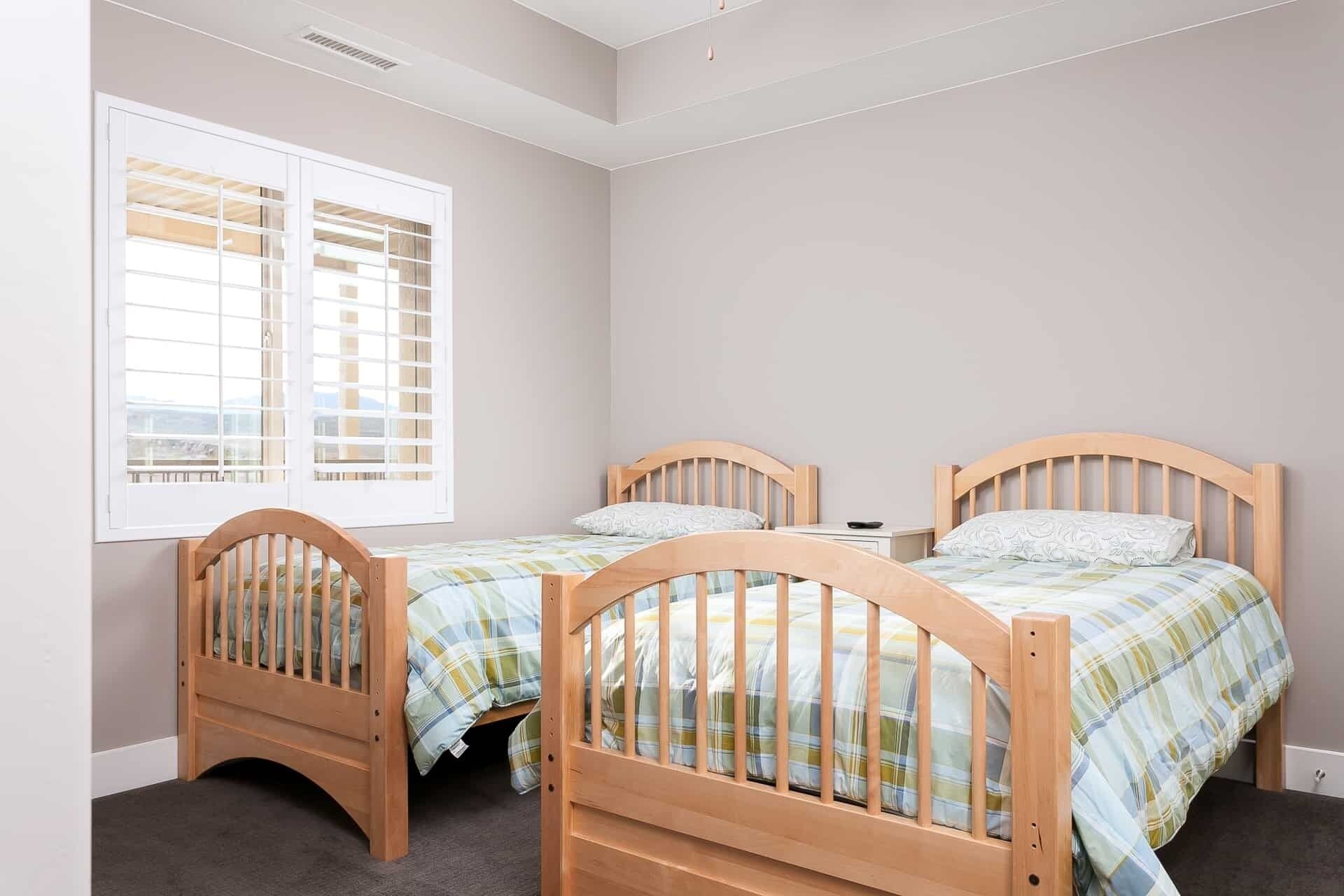 Quarto com duas camas de madeira, uma janela com persianas e uma pequena mesa de cabeceira.