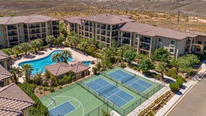 A resort with multiple buildings, a swimming pool, tennis courts, and a desert landscape in the background. - Stella's at Estancia by RedAwning (St. George)