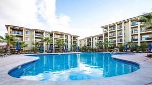 A swimming pool surrounded by a building with balconies, palm trees, and blue umbrellas. - Stella's at Estancia by RedAwning (St. George)