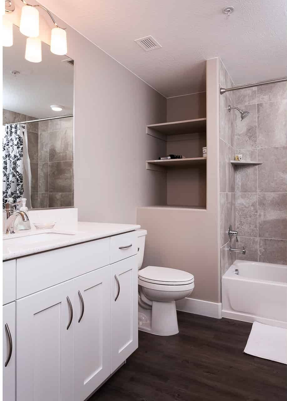 Et moderne badeværelse med et hvidt skab, toilet, bruser og badekar.