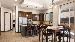 A modern kitchen with dark wooden cabinets, a central island with bar stools, and a dining table with chairs. - Coral Vista Villa by RedAwning (Washington)