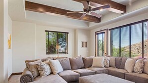 A spacious living room with a sectional sofa, ottoman, ceiling fan, and large windows offering a view of the outdoors. - Coral Vista Villa by RedAwning (Washington)